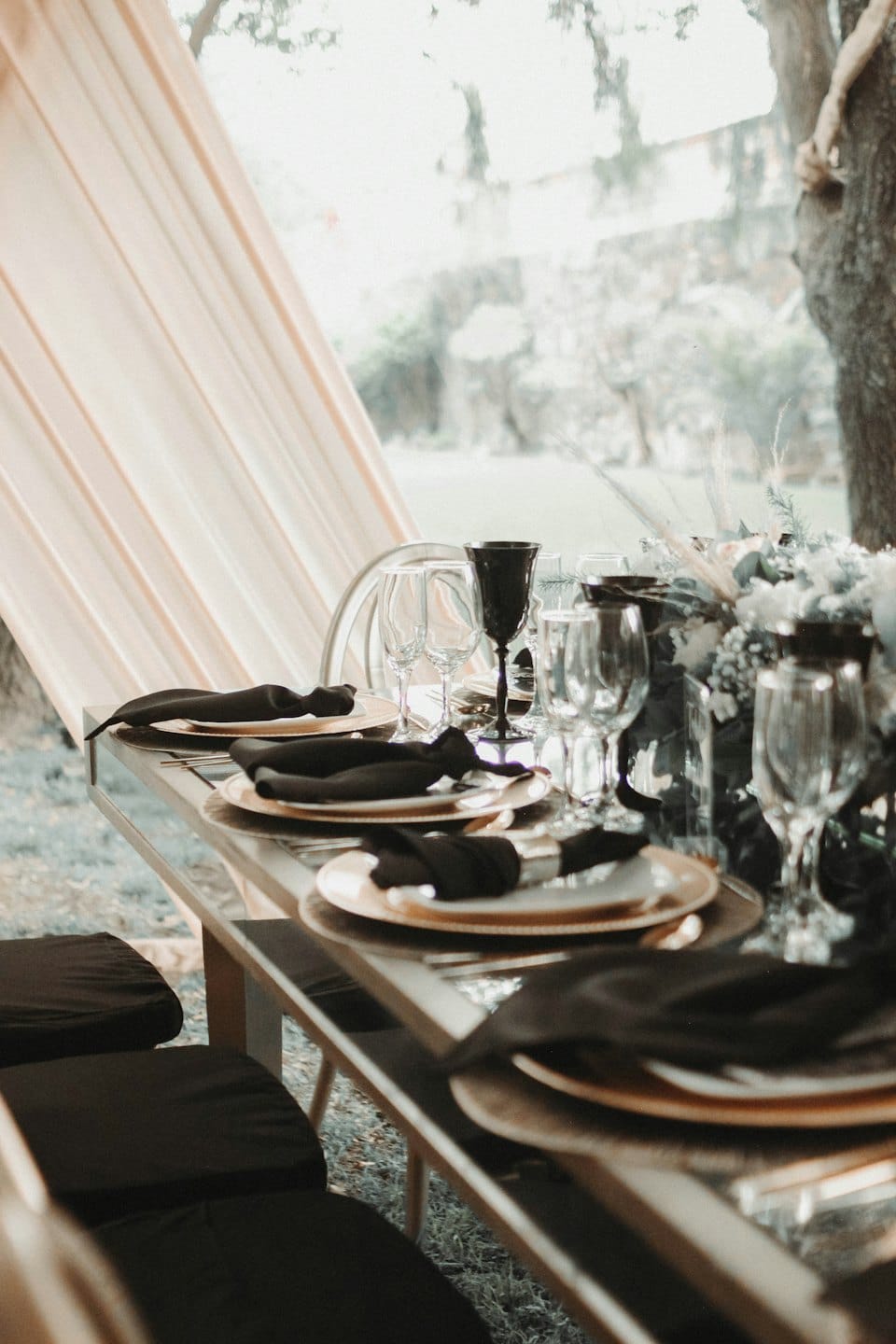 Elegant outdoor dining table set with gold chargers and floral centerpiece.